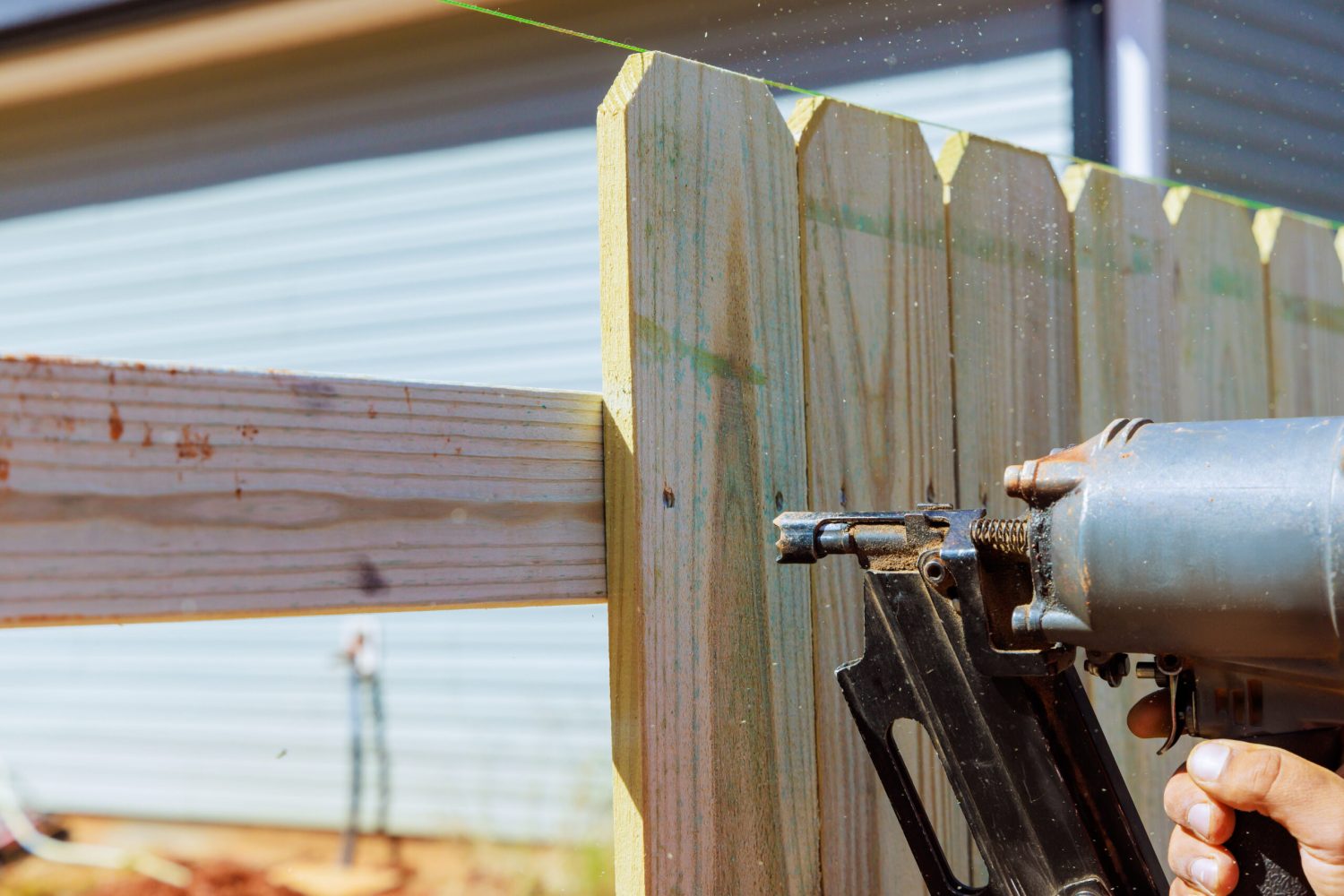 Nailer using air pneumatic gun to secure wooden plank fence during work