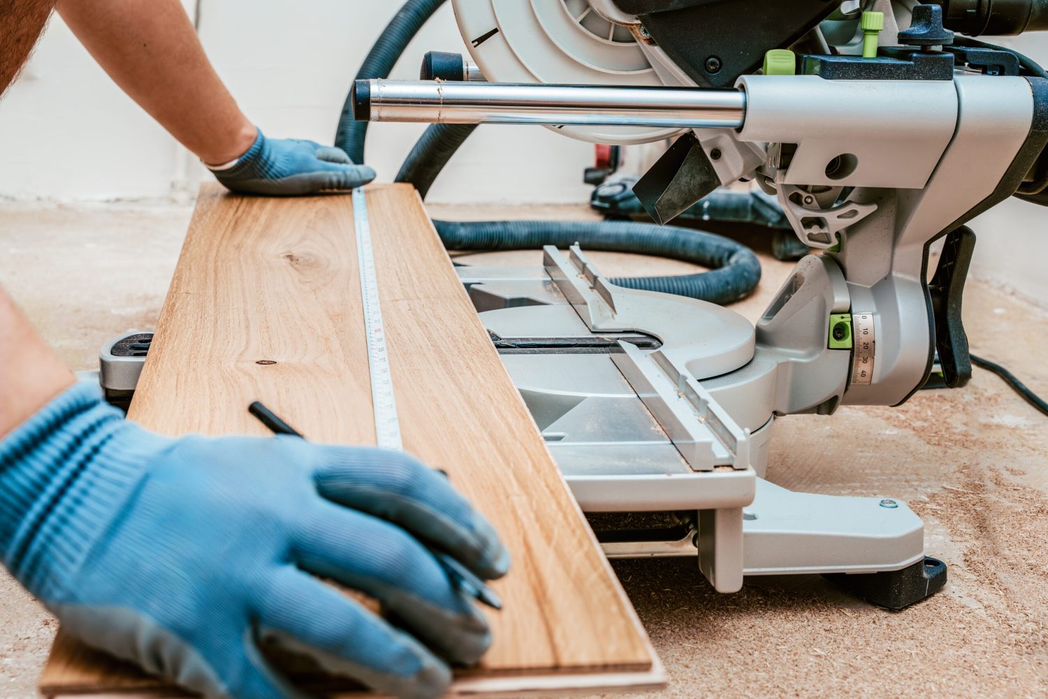 Worker in gloves measures wooden plank using tape measure, preparing to cut with circular saw for flooring installation